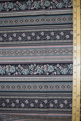 Stylized flowers and geometric designs in narrow border print. Muted colors of mauve, blue, taupe and black.