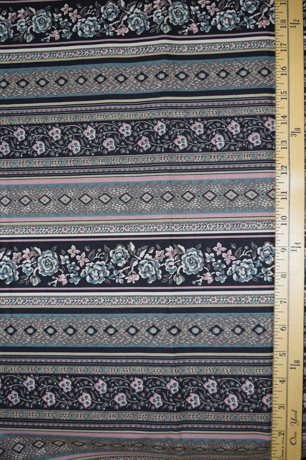 Stylized flowers and geometric designs in narrow border print. Muted colors of mauve, blue, taupe and black.