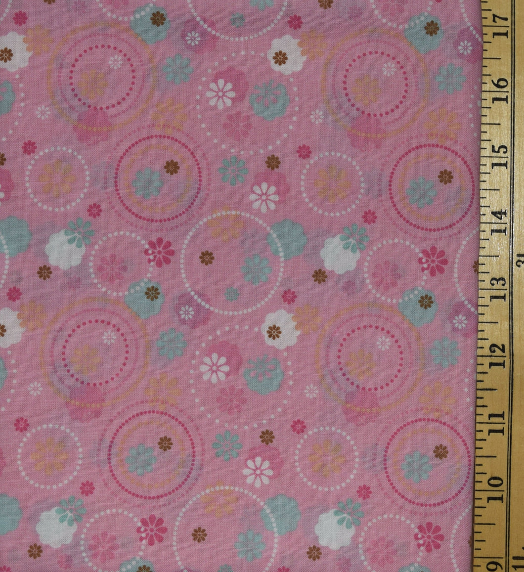 Circles drawn with dots in two shades of pink and white with small blossoms in teal, white, brown, pink, and yellow scattered overlapping over fabric.